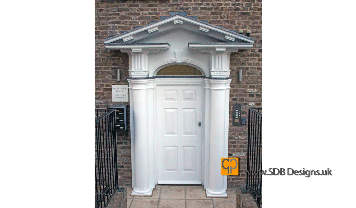 Triangular pediment portico doorway in white with large columns either side of a six field and raised panelled door with arched window light above